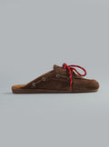 Brown suede shoe with red laces on a gray background