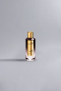 A sleek perfume bottle with a gold cap and label, featuring the fragrance name Aoud Vanille Dark Purple, set against a minimalistic grey background.