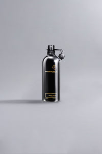 Sleek black metal bottle of Black Aoud Black fragrance by Montale, showcasing luxury perfume design with minimalist high fashion appeal against a neutral gray background.
