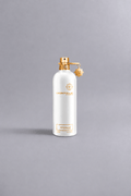 White Montale Paris perfume bottle with gold accents and charm, featuring the scent Mukhallat White on a neutral gray background, representing luxury fragrance packaging.