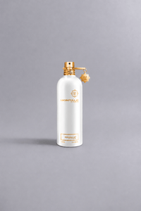 White Montale Paris perfume bottle with gold accents and charm, featuring the scent Mukhallat White on a neutral gray background, representing luxury fragrance packaging.