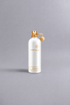 White Montale Paris perfume bottle with gold accents and charm, featuring the scent Mukhallat White on a neutral gray background, representing luxury fragrance packaging.