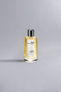 Bottle of Coco Vanille Yellow Dessin with golden liquid and sleek silver cap, set against a light grey background, evoking luxury and high fashion.