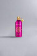 Bright pink luxury perfume bottle with gold intricate design and spray nozzle, labeled Crazy In Love Fuchsia, standing on a smooth neutral background.