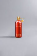 Sleek and elegant red bottle of Oud Tobacco Red perfume with gold spray top and charm, presented against a minimalist gray background.