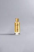 Elegant glass bottle of Sicily Gold perfume with a golden cap, filled with a warm golden liquid, placed on a smooth light gray surface.