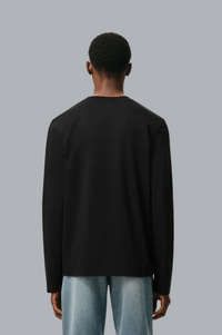 A man viewed from the back wearing a black long-sleeve crewneck shirt and light blue jeans, set against a solid gray background.