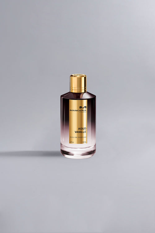 A sleek bottle of Aoud Vanille Dark Purple fragrance with a gradient dark purple to clear glass design and a shiny gold cap against a light gray background.