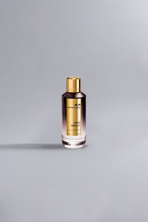 A sleek perfume bottle with a gold cap and label, featuring the fragrance name Aoud Vanille Dark Purple, set against a minimalistic grey background.