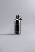 Sleek black metal bottle of Black Aoud Black fragrance by Montale, showcasing luxury perfume design with minimalist high fashion appeal against a neutral gray background.