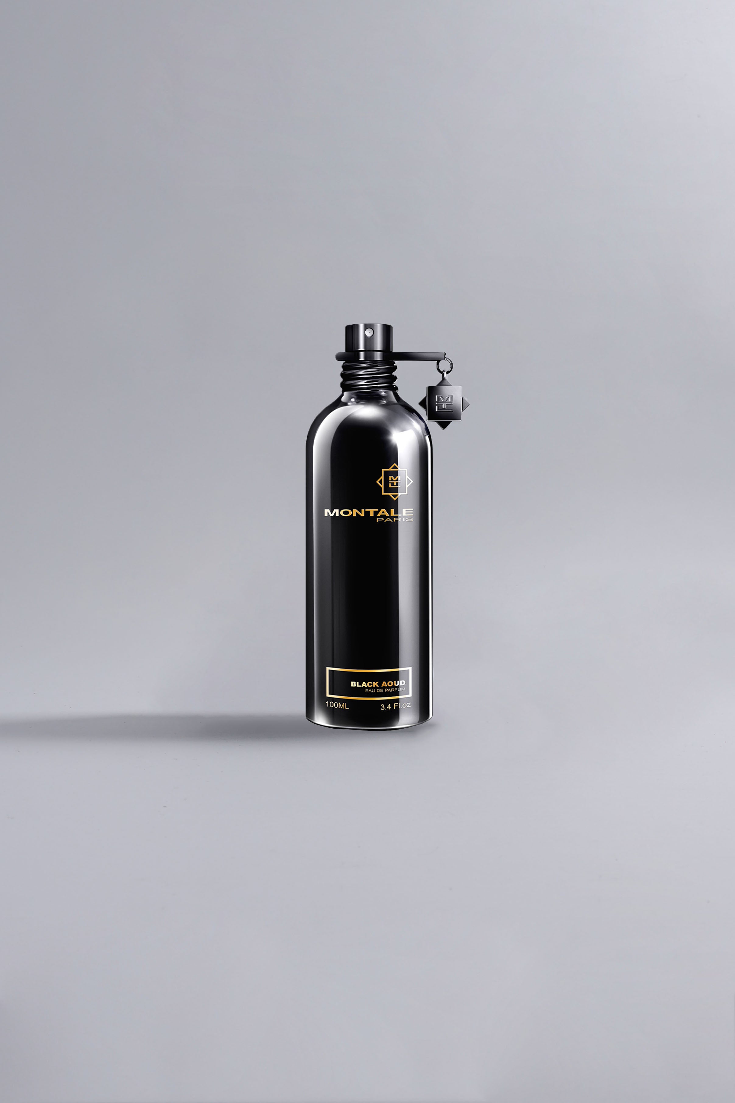 Sleek black metal bottle of Black Aoud Black fragrance by Montale, showcasing luxury perfume design with minimalist high fashion appeal against a neutral gray background.