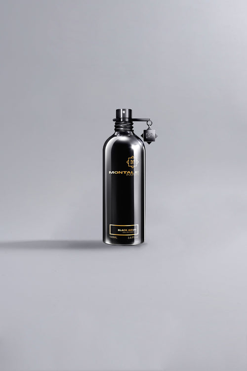 Sleek black metal bottle of Black Aoud Black fragrance by Montale, showcasing luxury perfume design with minimalist high fashion appeal against a neutral gray background.