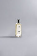 Clear glass perfume bottle with pale yellow liquid labeled Mancera Cedrat Boise, placed on a smooth neutral gray surface, Cedrat Boise Yellow Dessin.