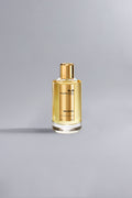 Clear glass bottle of Holidays Gold perfume with golden liquid and gold cap on a neutral gray background, showcasing a luxury fragrance product.