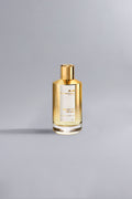 Melody Of The Sun Gold perfume bottle with a sleek golden cap and elegant transparent glass design, set against a minimalist light gray background.