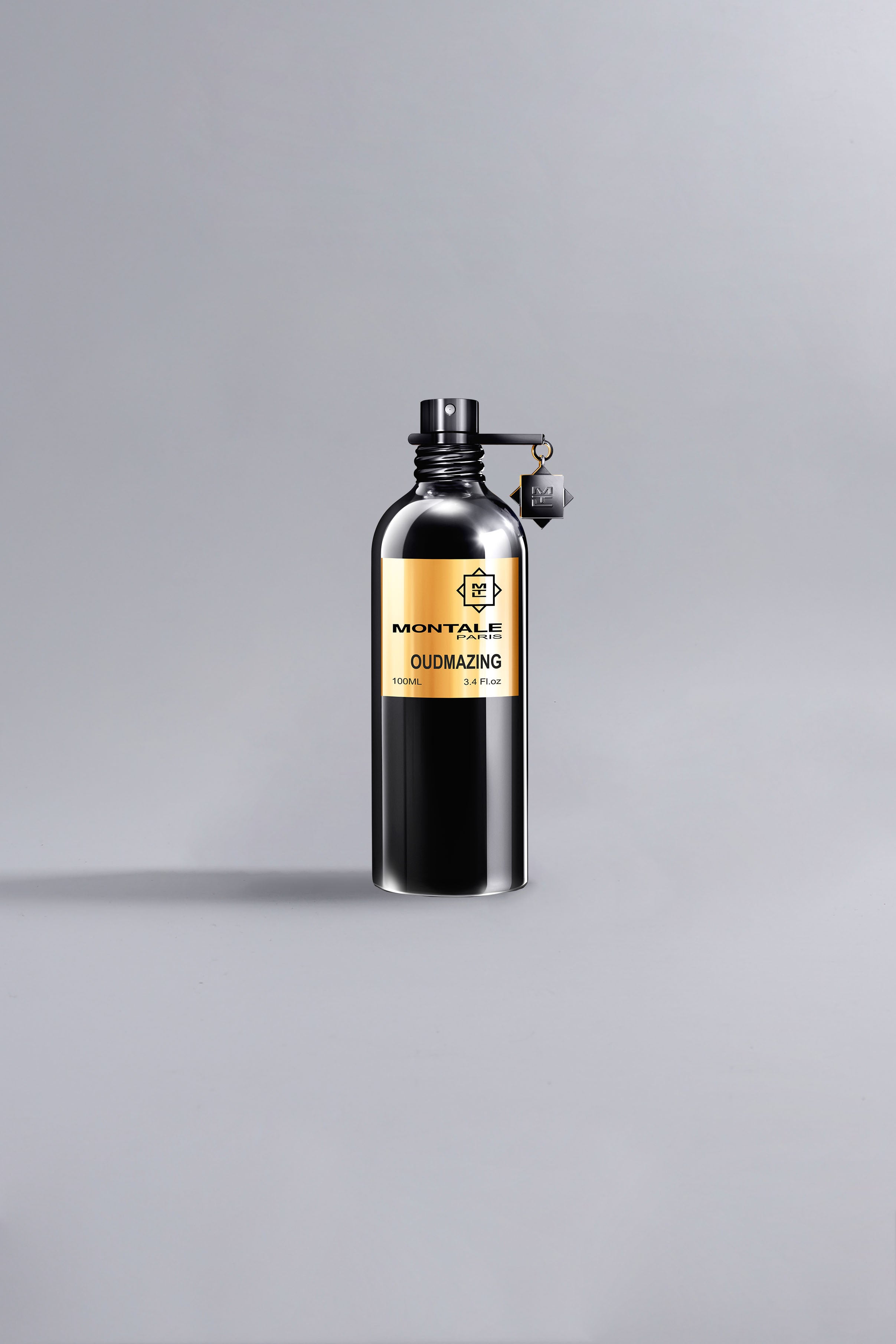 Sleek black bottle with gold label displaying Oudmazing Black, a luxury high fashion fragrance from Maastricht, standing on a neutral light gray background.