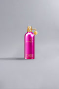 A vibrant fuchsia pink luxury perfume bottle with gold accents and a small gold charm against a soft gray background, labeled Roses Musk Fuchsia.