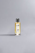 Glass bottle of Roses Vanille Ocher perfume with golden liquid and silver cap, set against a soft gray background, showcasing luxury and elegance.