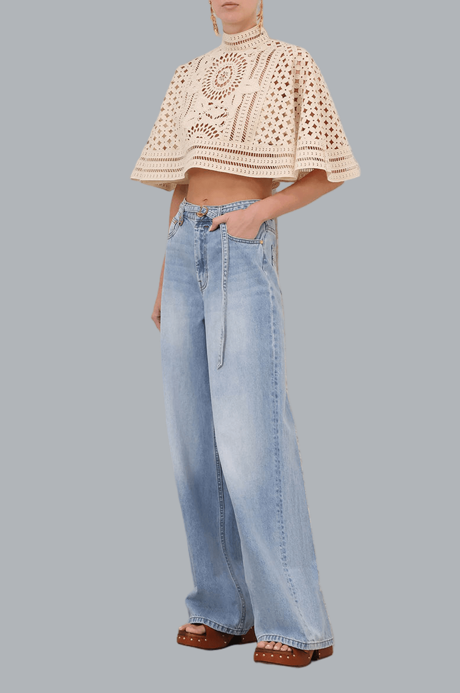 Person wearing a beige crochet top and light blue jeans on a gray background